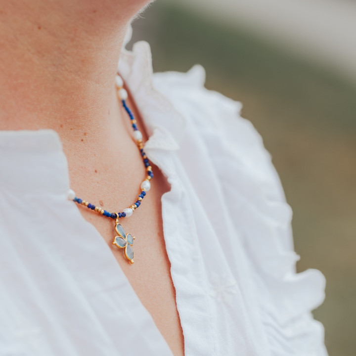 Jeune femme portant un collier Murmures Precieux® Bijoux créé avec l'alphabet Morse à murmures secrets en pierre fine lapis-lazuli, perles de culture, enfilé à la main avec un pendentif en croix bleu clair