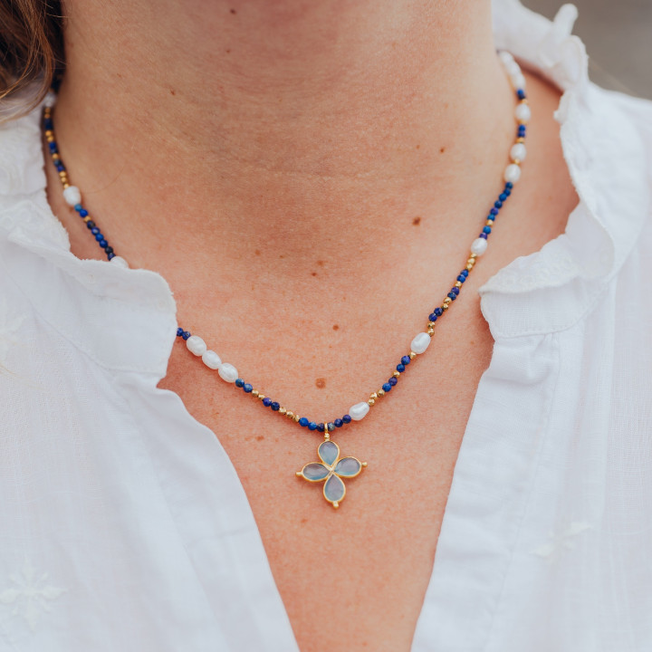 Jeune femme portant un collier Murmures Precieux® Bijoux créé avec l'alphabet Morse à murmures secrets en pierre fine lapis-lazuli, perles de culture, enfilé à la main avec un pendentif en croix bleu clair